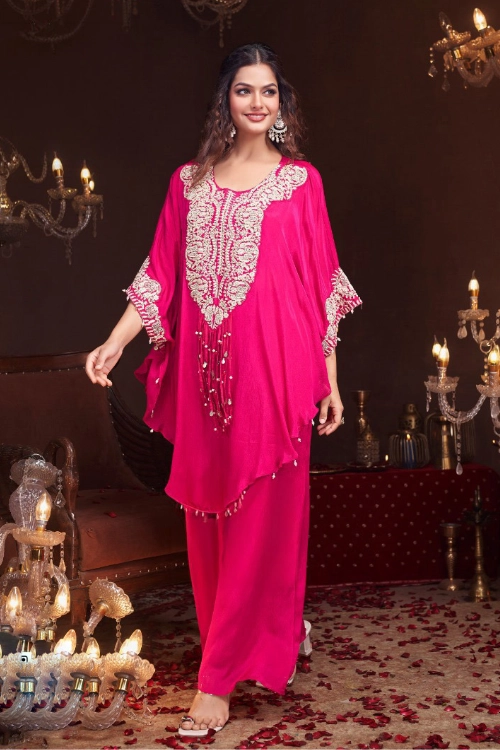 1 Vibrant Pink Chinon Palazzo Set with Silver Embroidery: A woman posing in a premium 3-piece ethnic ensemble featuring a short tunic with intricate silver handwork on the neckline and hem, paired with wide-leg palazzo trousers and a sheer dupatta.