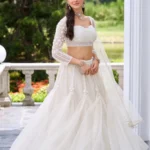 White Embellished Net Lehenga Set: A woman in a premium 3-piece wedding outfit featuring a voluminous tiered net lehenga, an intricately embroidered corset-style blouse, and a sheer net dupatta—ideal for engagement parties and modern bridesmaids