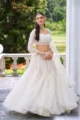White Embellished Net Lehenga Set: A woman in a premium 3-piece wedding outfit featuring a voluminous tiered net lehenga, an intricately embroidered corset-style blouse, and a sheer net dupatta—ideal for engagement parties and modern bridesmaids