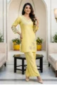 yellow shimmer kurta set with floral embellishments on the V-neck and hem. The outfit features contemporary cut-out sleeve detailing and matching wide-leg trousers, set against a luxurious indoor architectural background.