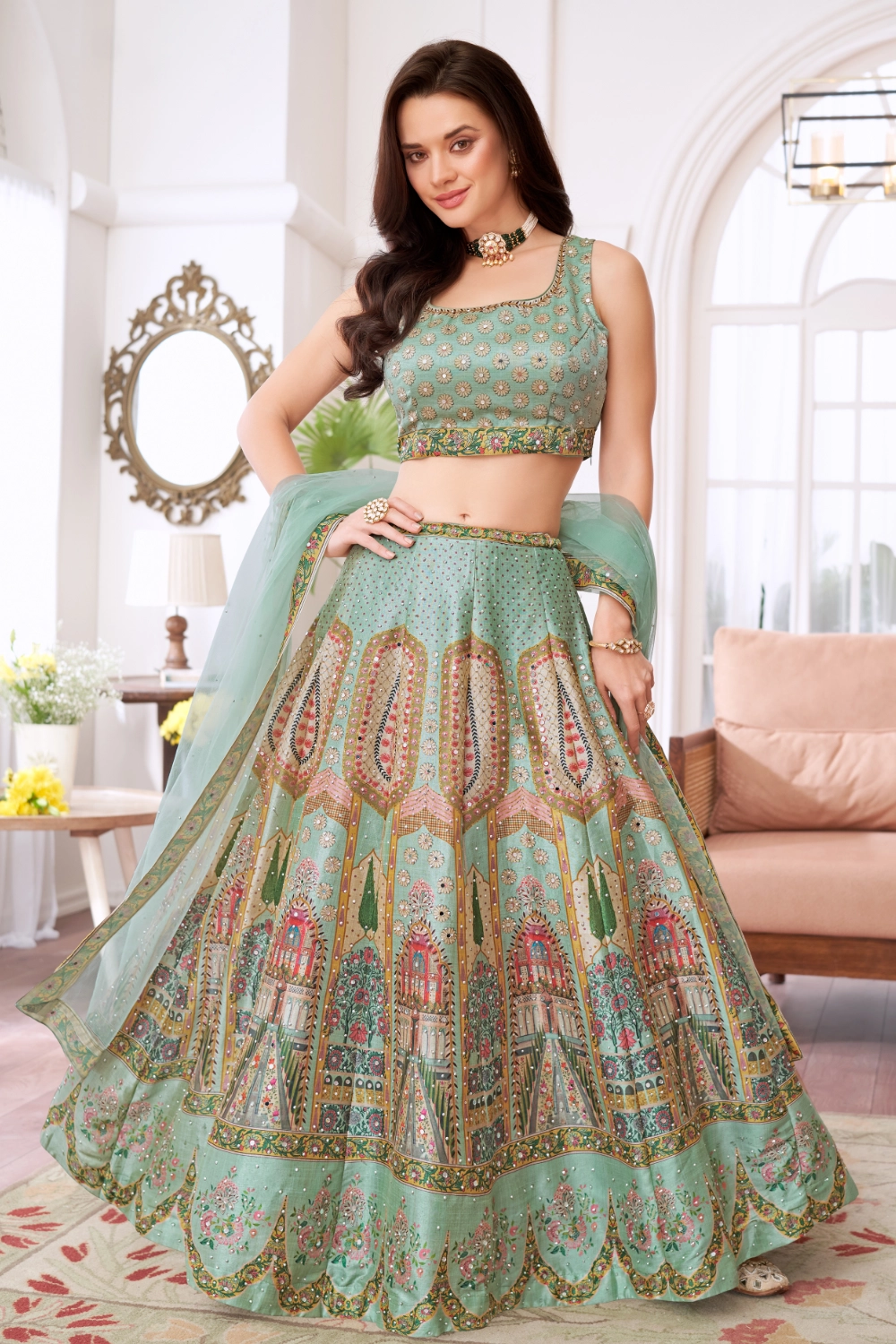 Mint Green Printed Chanderi Lehenga Choli Set Full view of a woman wearing a mint green choli lehenga set. The lehenga skirt is unique, featuring a digital architectural print of historic Indian archways and structures within patterned panels, combined with fine embroidery and sequin work. The matching mint green choli has mirror work