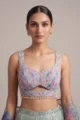 A model wearing a luxurious sequined georgette lehenga in light green, accented with bold blue botanical prints.