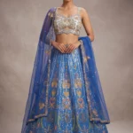Designer blue lehenga choli for luxury wedding guests featuring intricate gold mirror work and a sheer dupatta