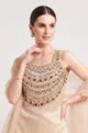 Close-up view of the dense multi-tiered golden beadwork and emerald green stone accents on the cream silk tunic.