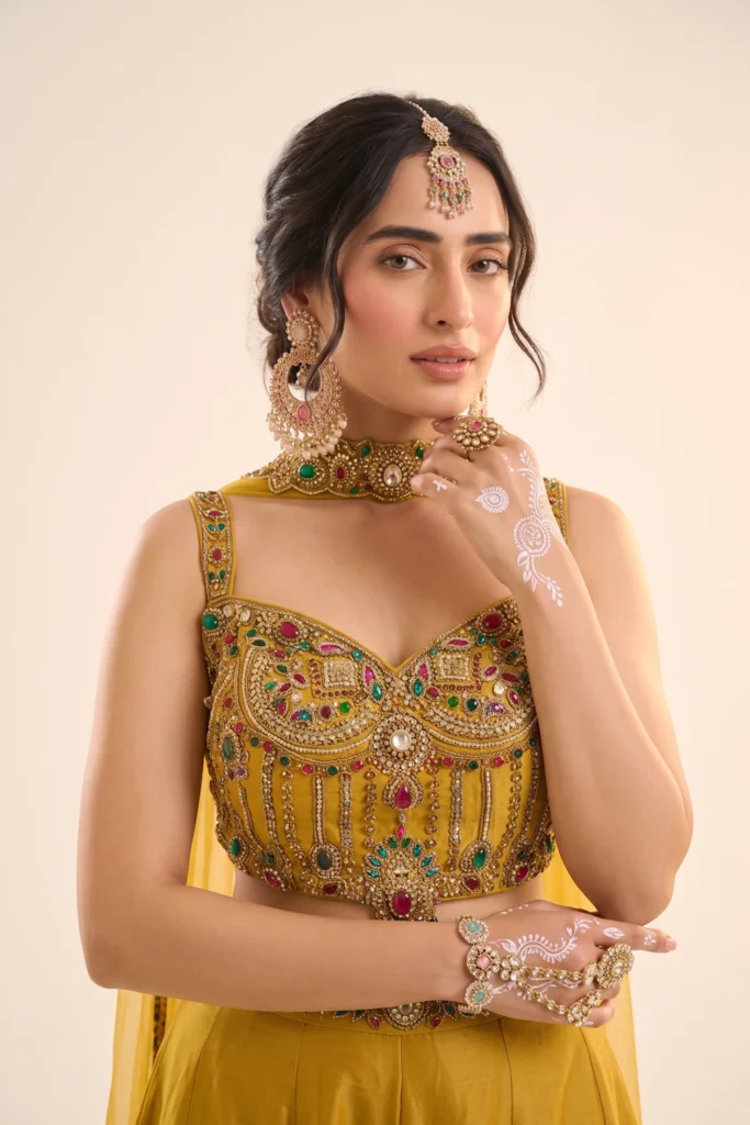 Close-up view of the dense multi-colored stone work, bead embroidery, and hanging jewel pendant on the yellow shimmer choli.