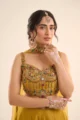 Close-up view of the dense multi-colored stone work, bead embroidery, and hanging jewel pendant on the yellow shimmer choli.